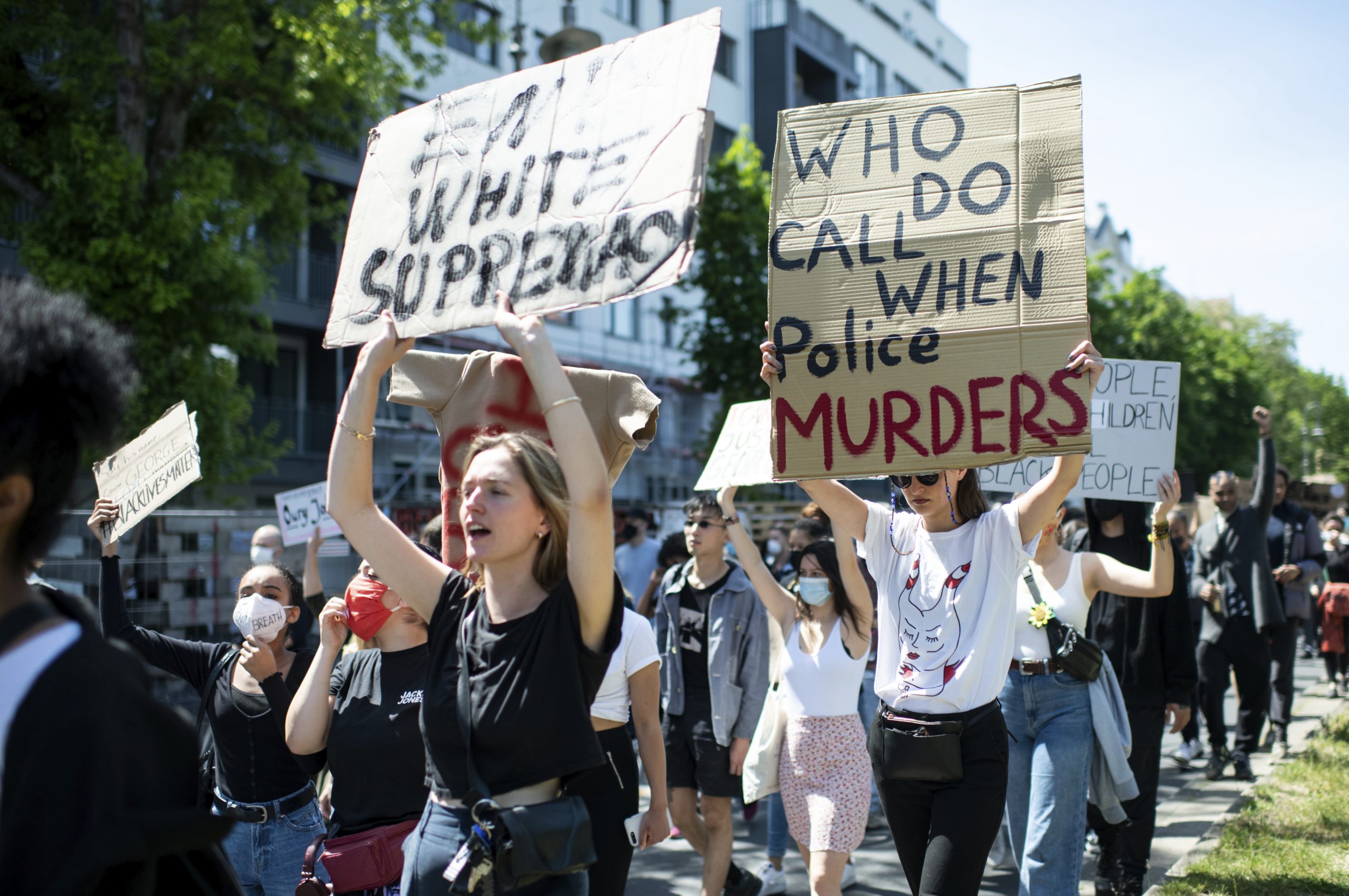 People protest in Berlin, Germany, Sunday, May 31, 2020 after the violent death of the African-American George Floyd by a white policeman in the USA against racism and police violence, among other things with a sign "Who do call when police murders" (Bernd von Jutrczenka/dpa via AP)
